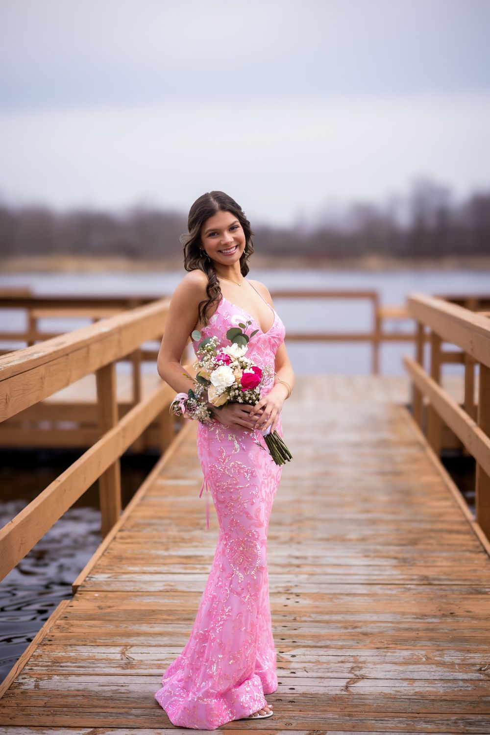A person in a fitted pink sequin dress holds a bouquet while posing on a wooden dock.