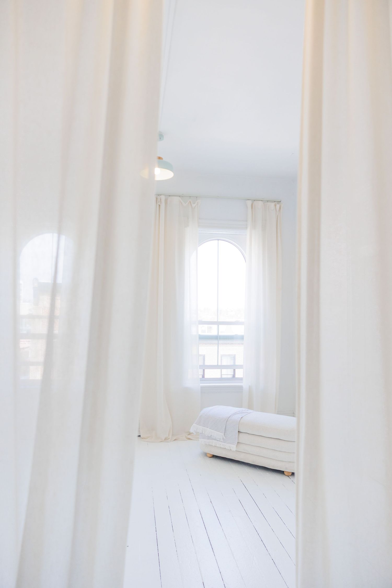 Clean white folded towels and linens with knit blanket on gray surface next to sheer curtains.