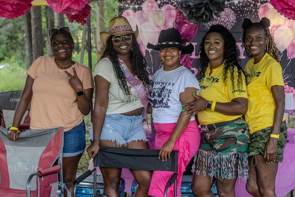 A group of friends gather together at an outdoor event decorated with pink and purple floral accents.
