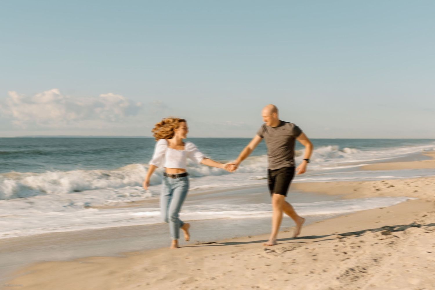 A candid action shot of a couple running barefoot along the shoreline, filled with movement and joy.