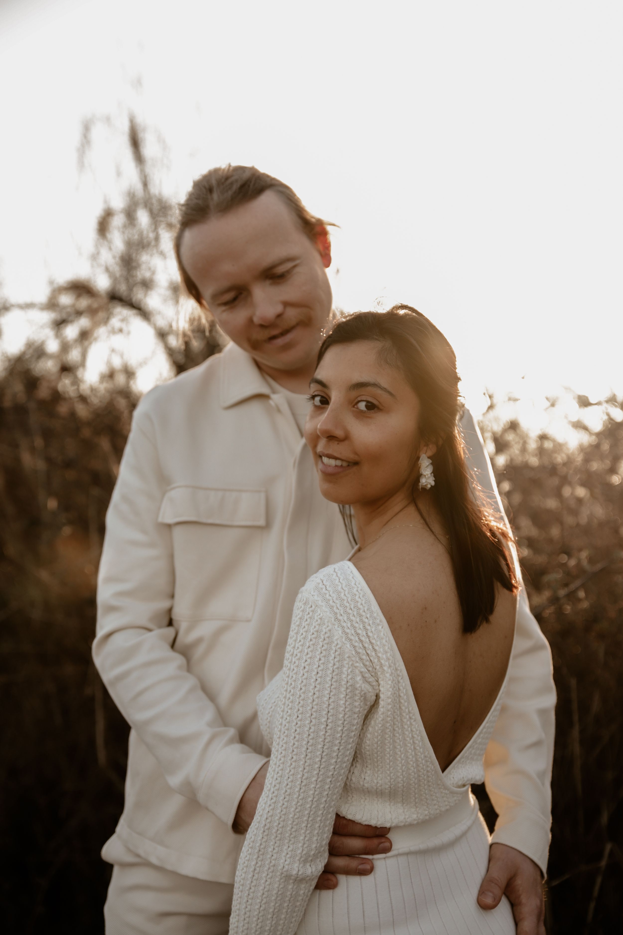 Couple in elegant white outfits posing during golden hour portrait session.