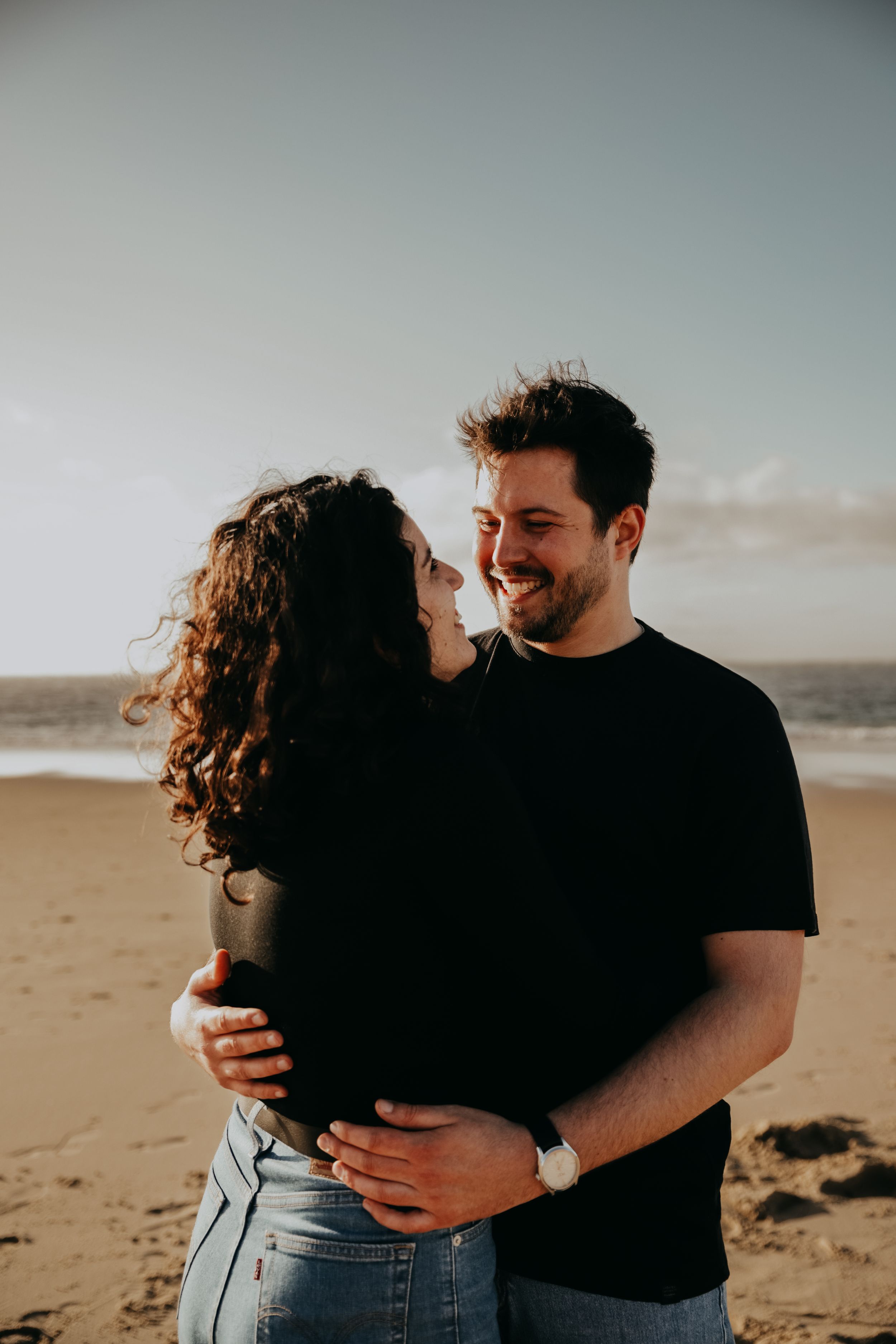 Romantic couple embracing and smiling at each other on beach at golden hour.