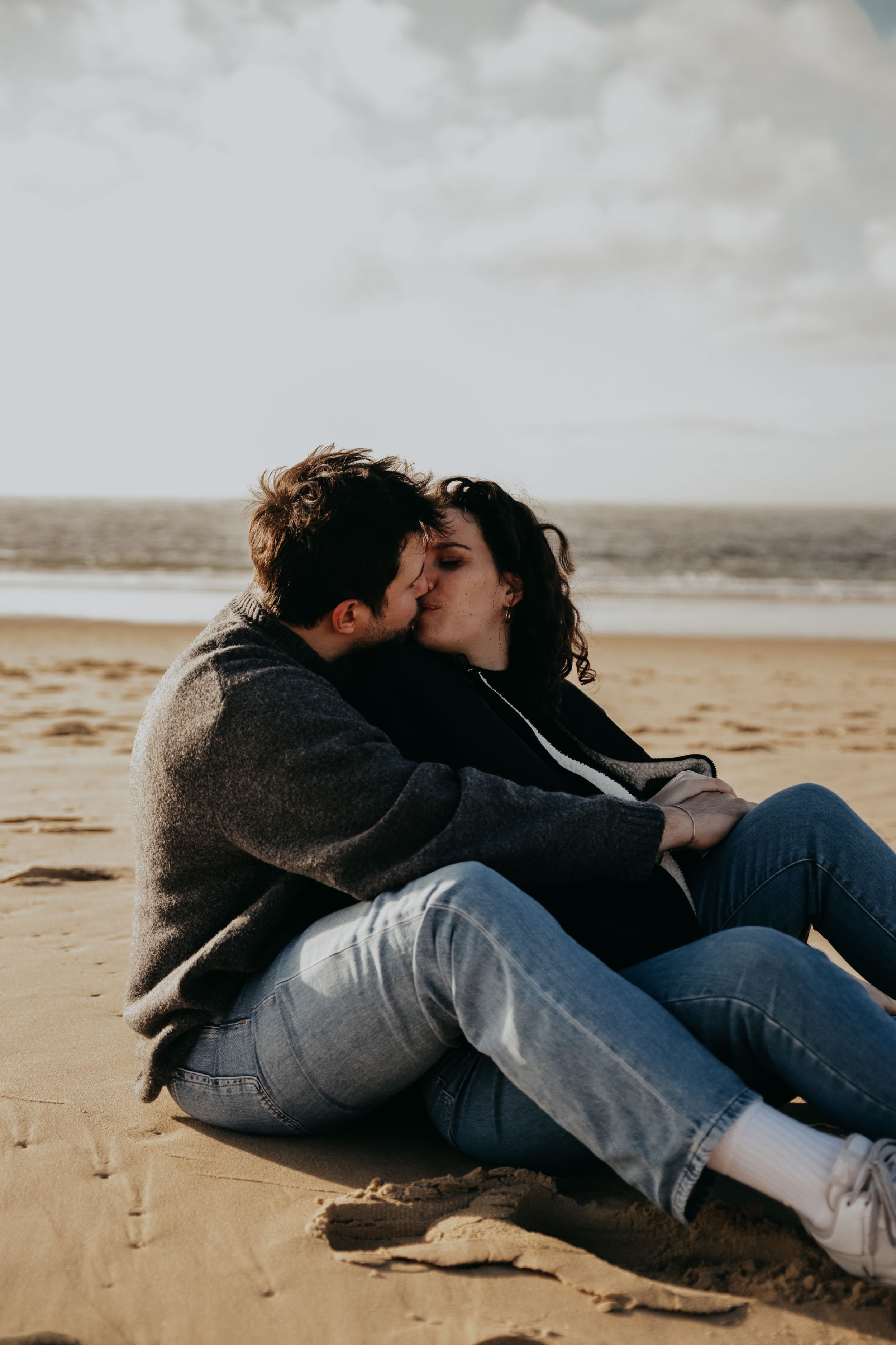 Couple kissing while sitting together on sandy beach during sunset.