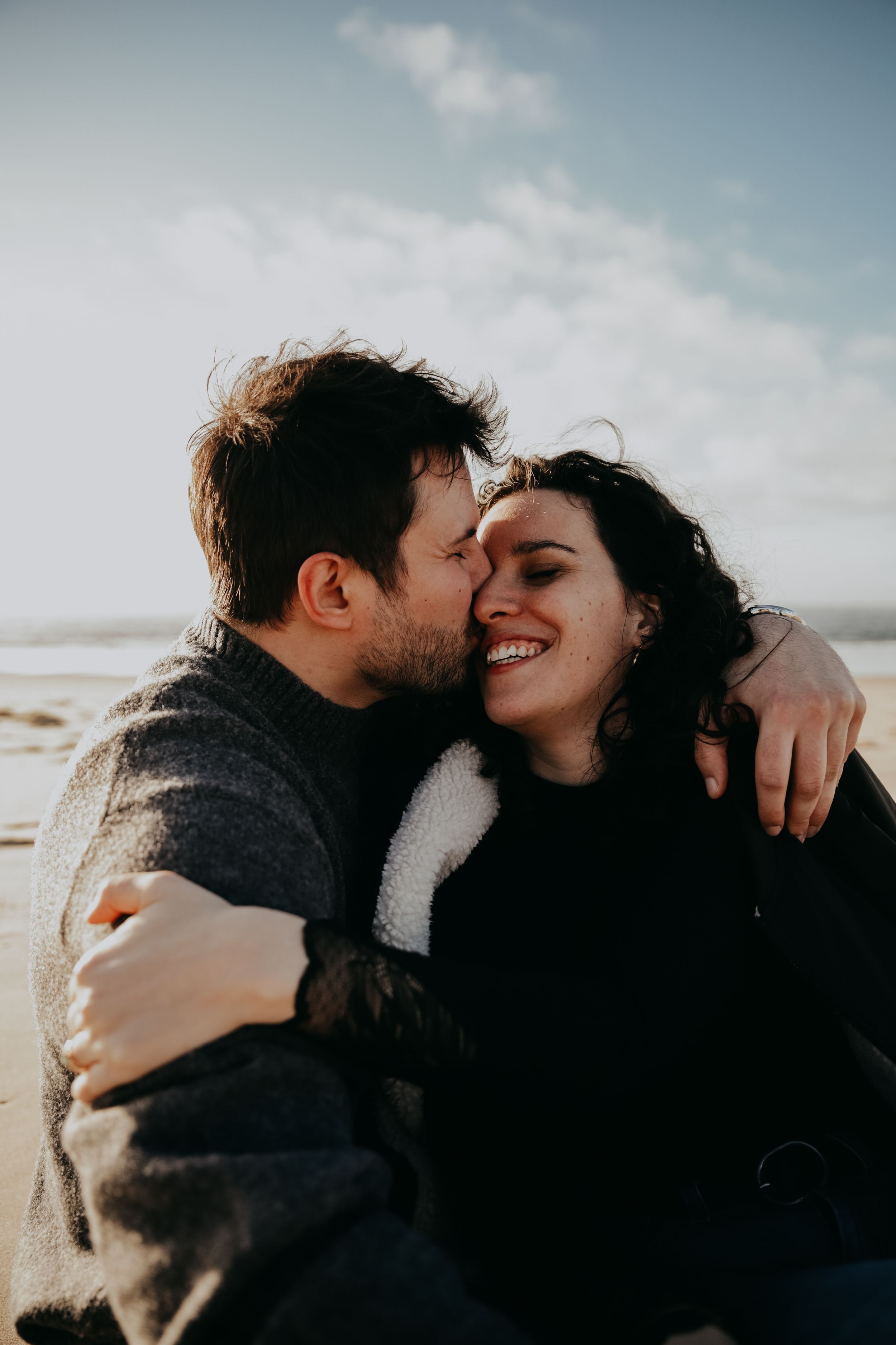 Couple sharing tender moment and laughing together on windy beach.