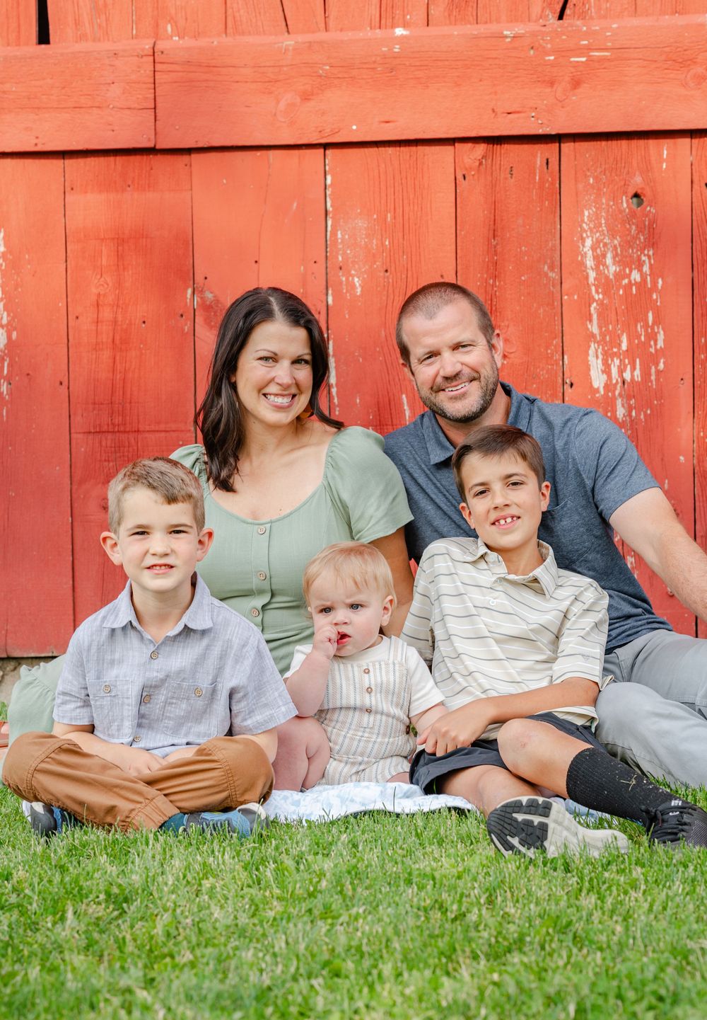 family sitting on ground in front of barn