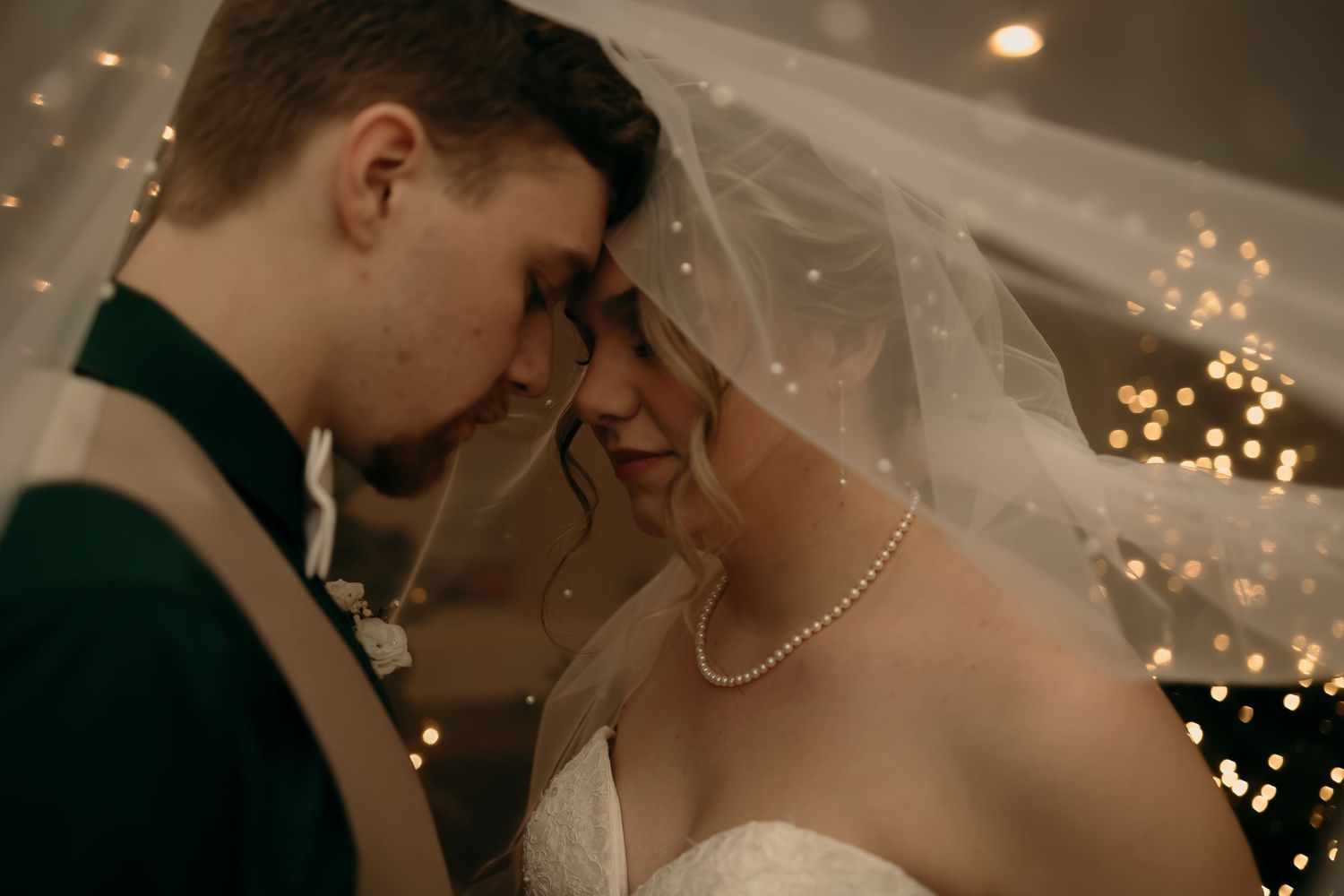 A romantic wedding moment captured in warm lighting with twinkling bokeh lights and a delicate veil in the background.