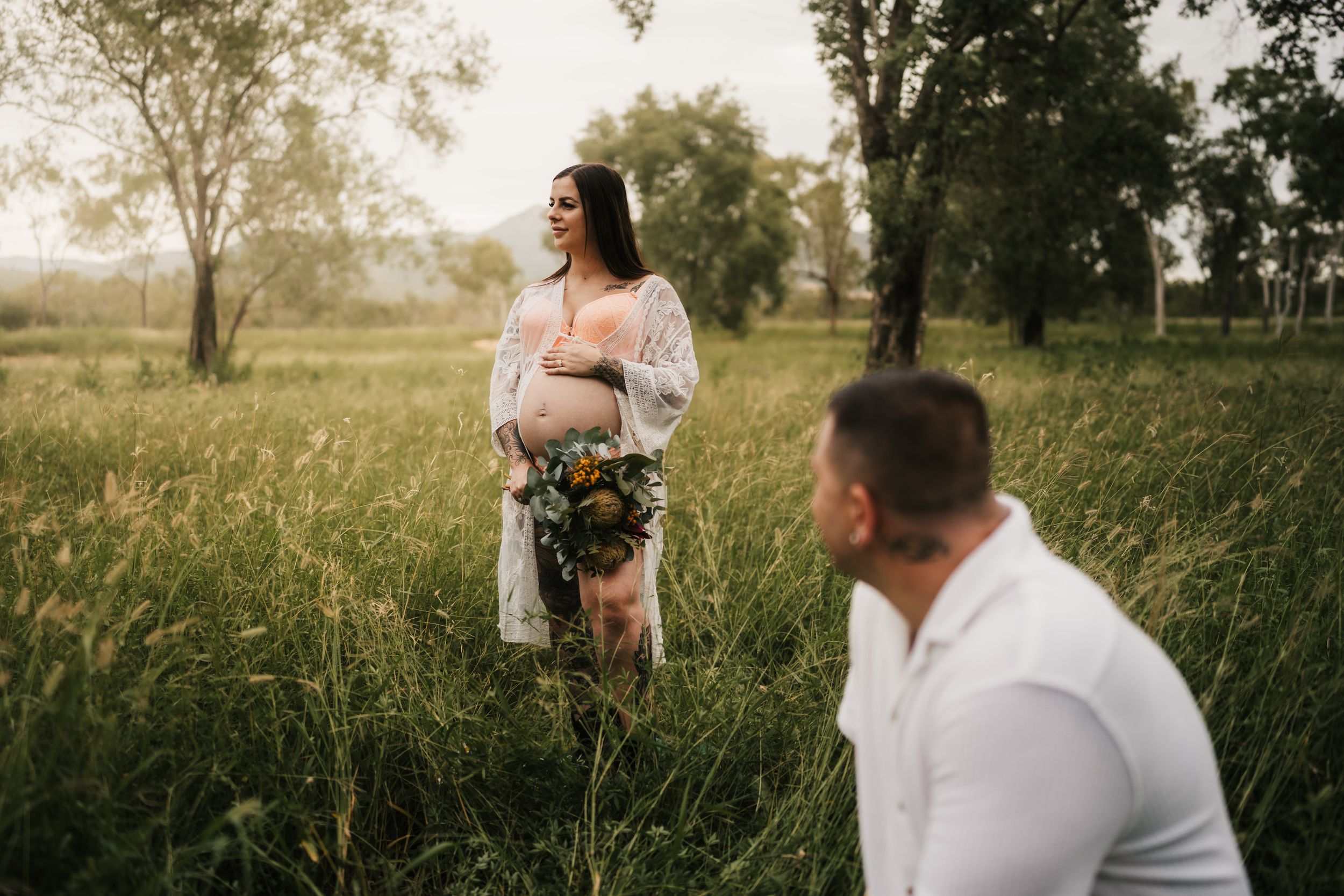 A dreamy maternity photoshoot in a sunlit meadow with tall grass and trees in the background.