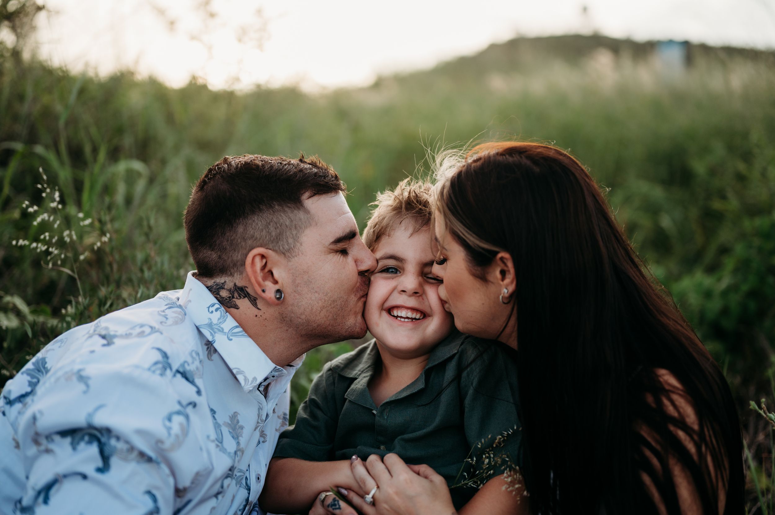 A family sharing a tender moment together outdoors during golden hour in a grassy meadow.