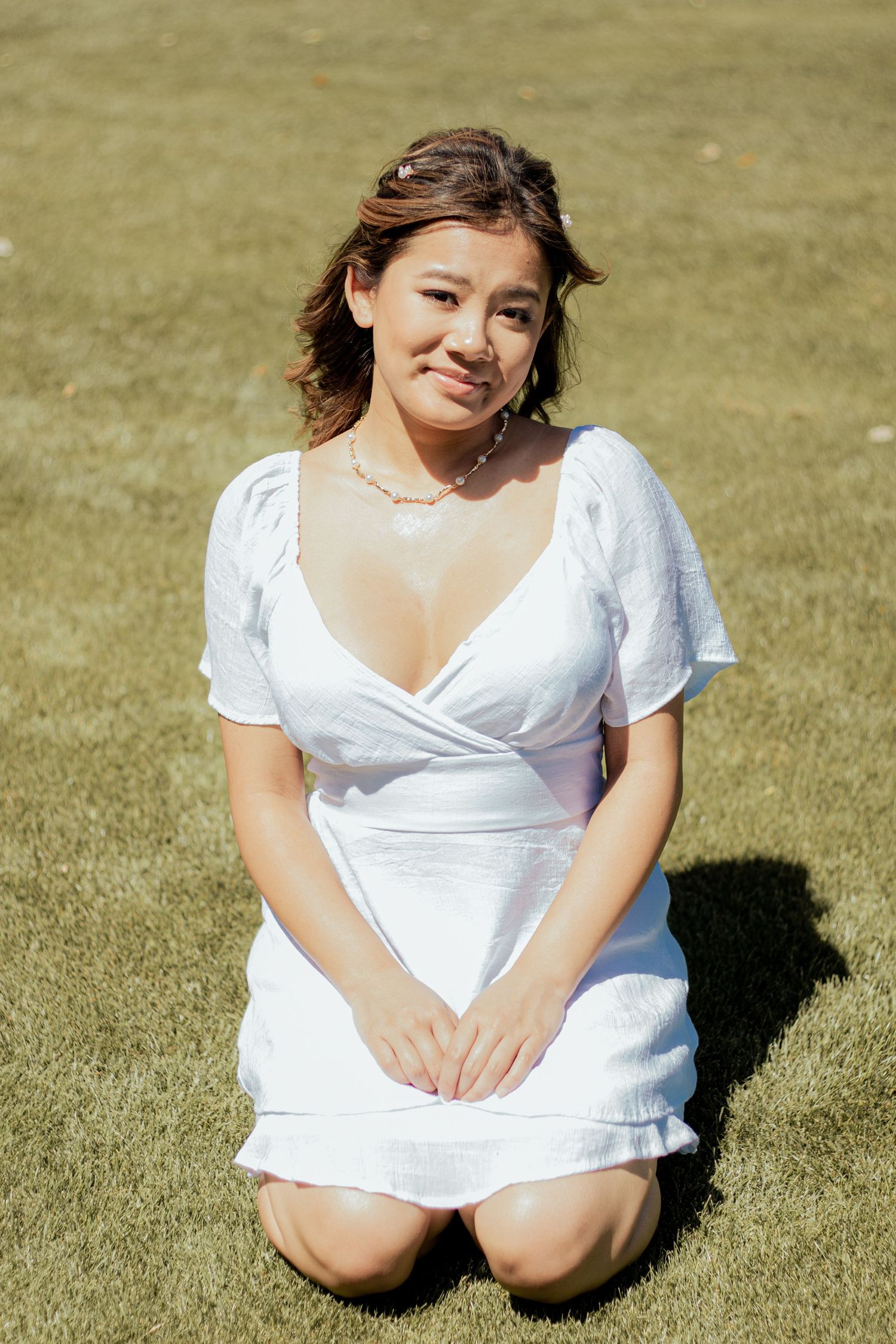 A person in a white summer dress with puff sleeves kneels on grass under bright sunlight.