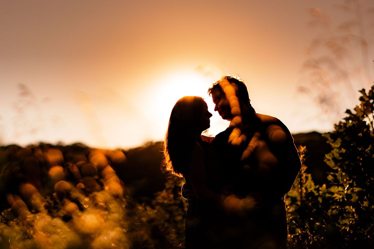 Dramatic sunset silhouette of couple embracing with golden sky background.