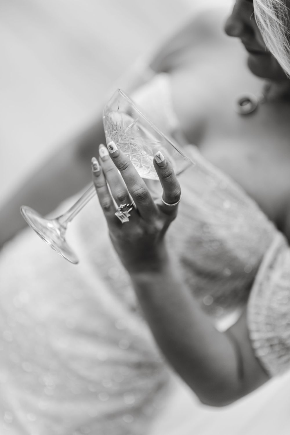 Close-up black and white photo of hand holding champagne glass with engagement ring sparkling on finger.