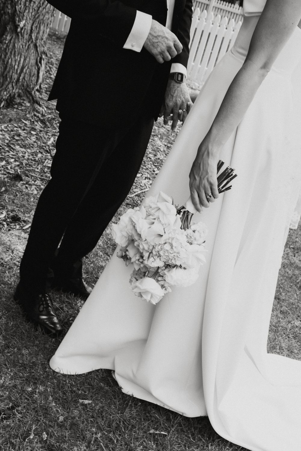 Black and white wedding photo showing close-up of bride and groom's formal attire and a delicate bouquet.