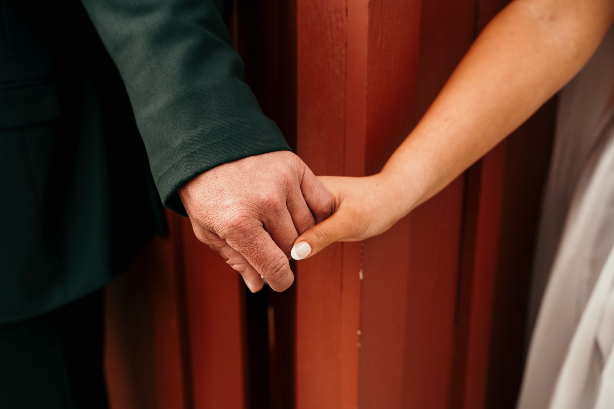 Two hands clasp together in a tender moment against a reddish background.