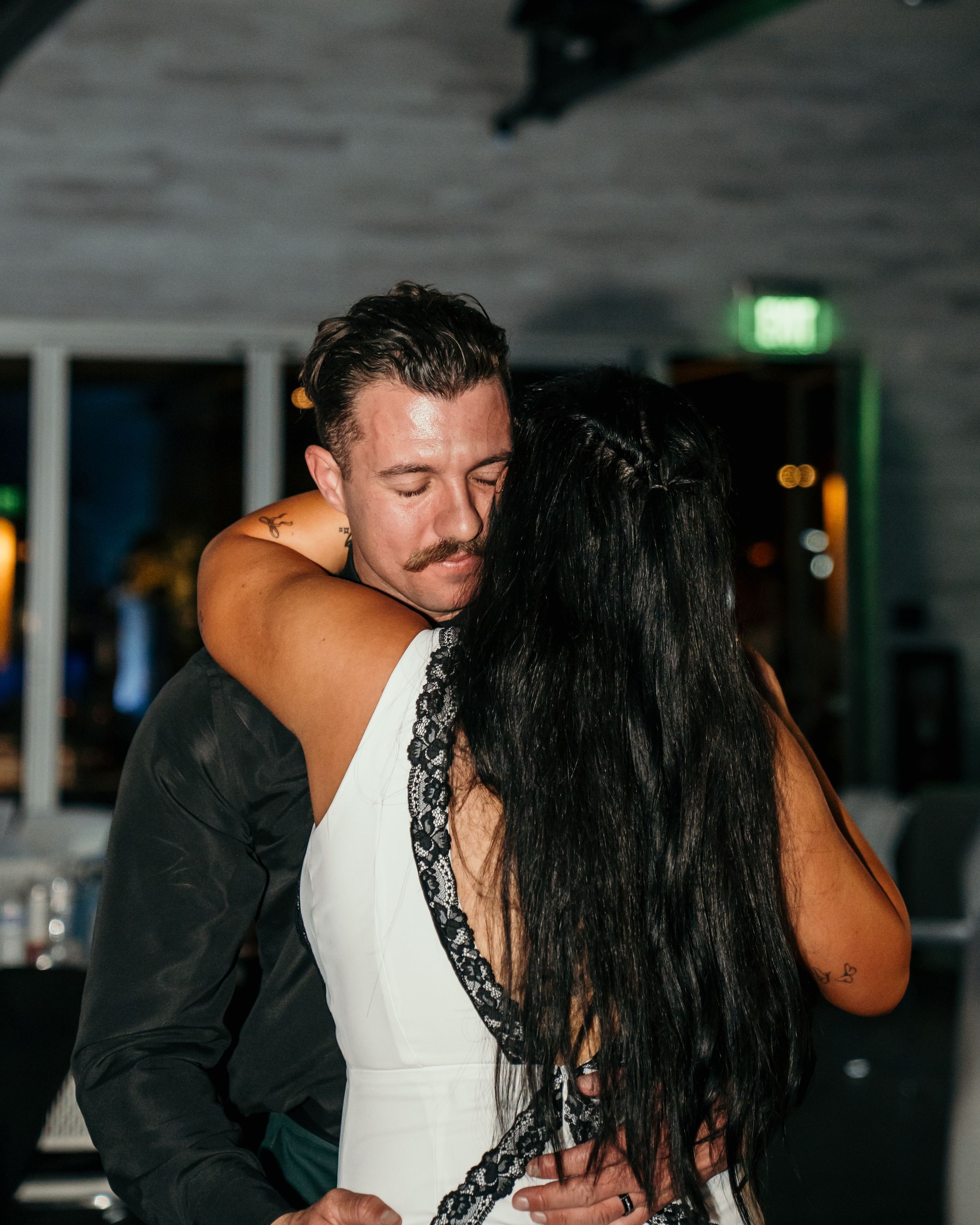 A couple shares an intimate dance together in a dimly lit venue with a soft glow of green lighting.