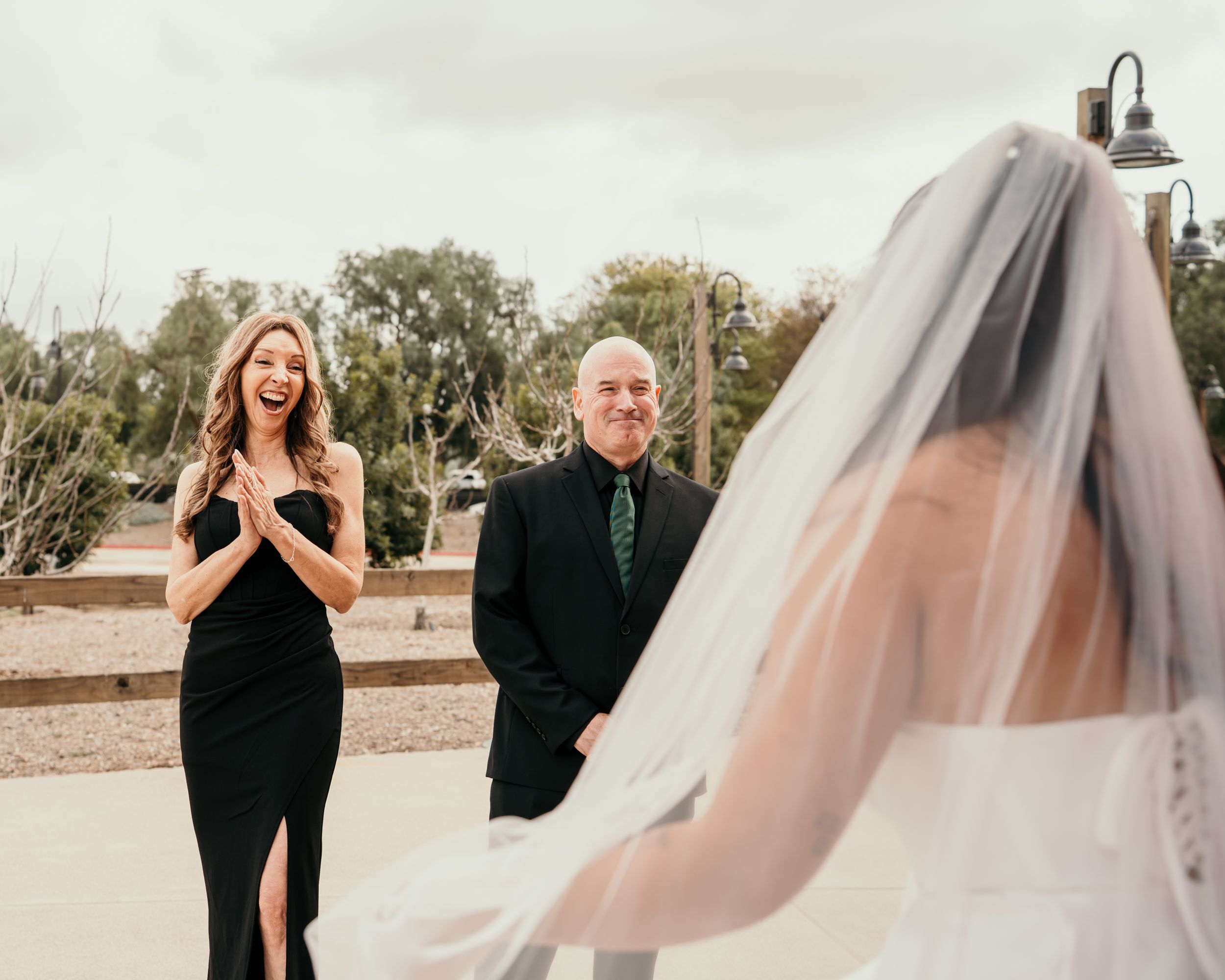 Wedding guests share an emotional moment as a bride in a flowing veil arrives at an outdoor ceremony.