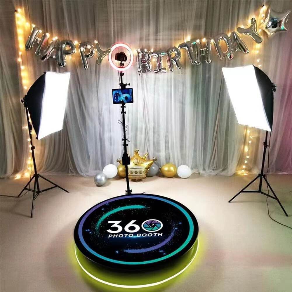 Photo booth setup with softbox lights, birthday banner, and illuminated circular 360 platform for photography.