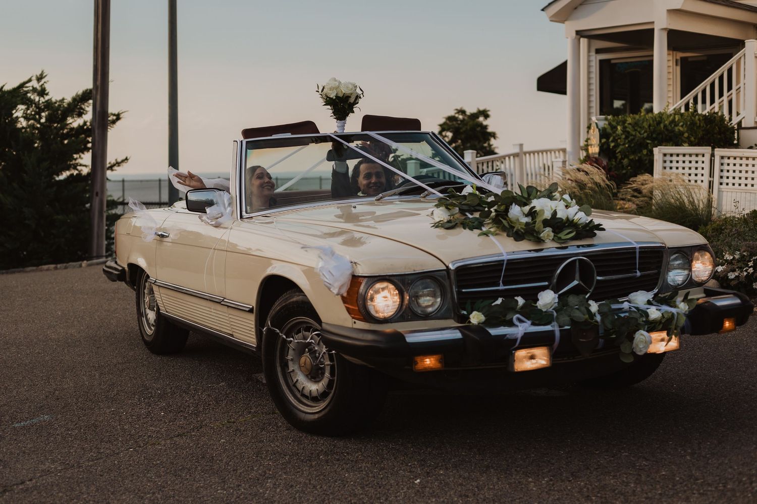 Classic white Mercedes-Benz convertible decorated with flowers for a wedding sits parked at sunset.