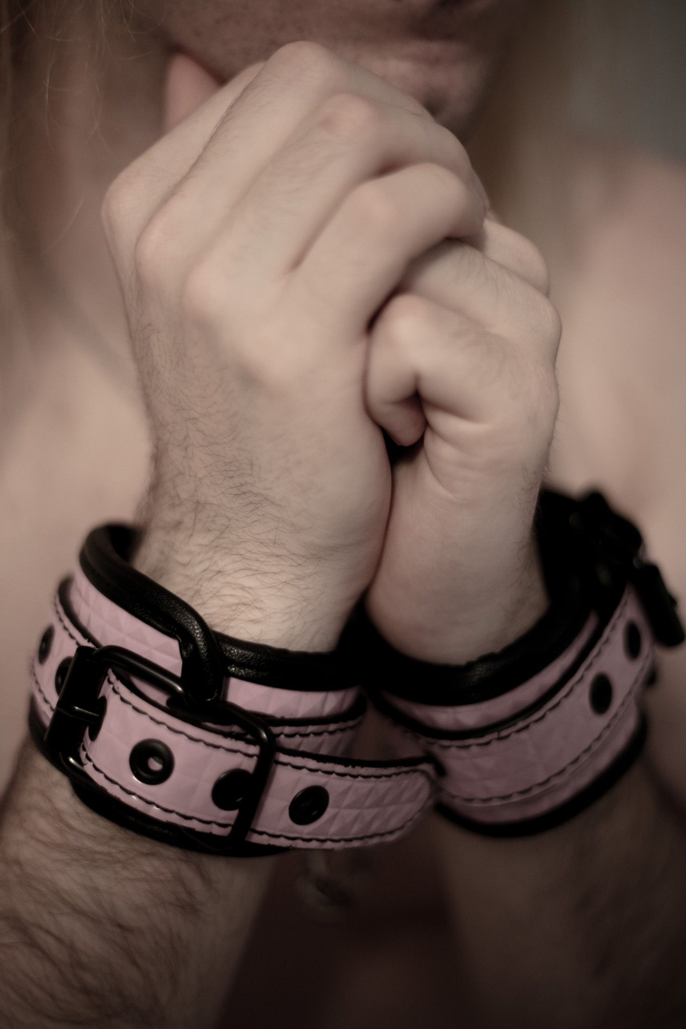 Close-up of hands bound with pink leather cuffs in soft monochromatic tones.