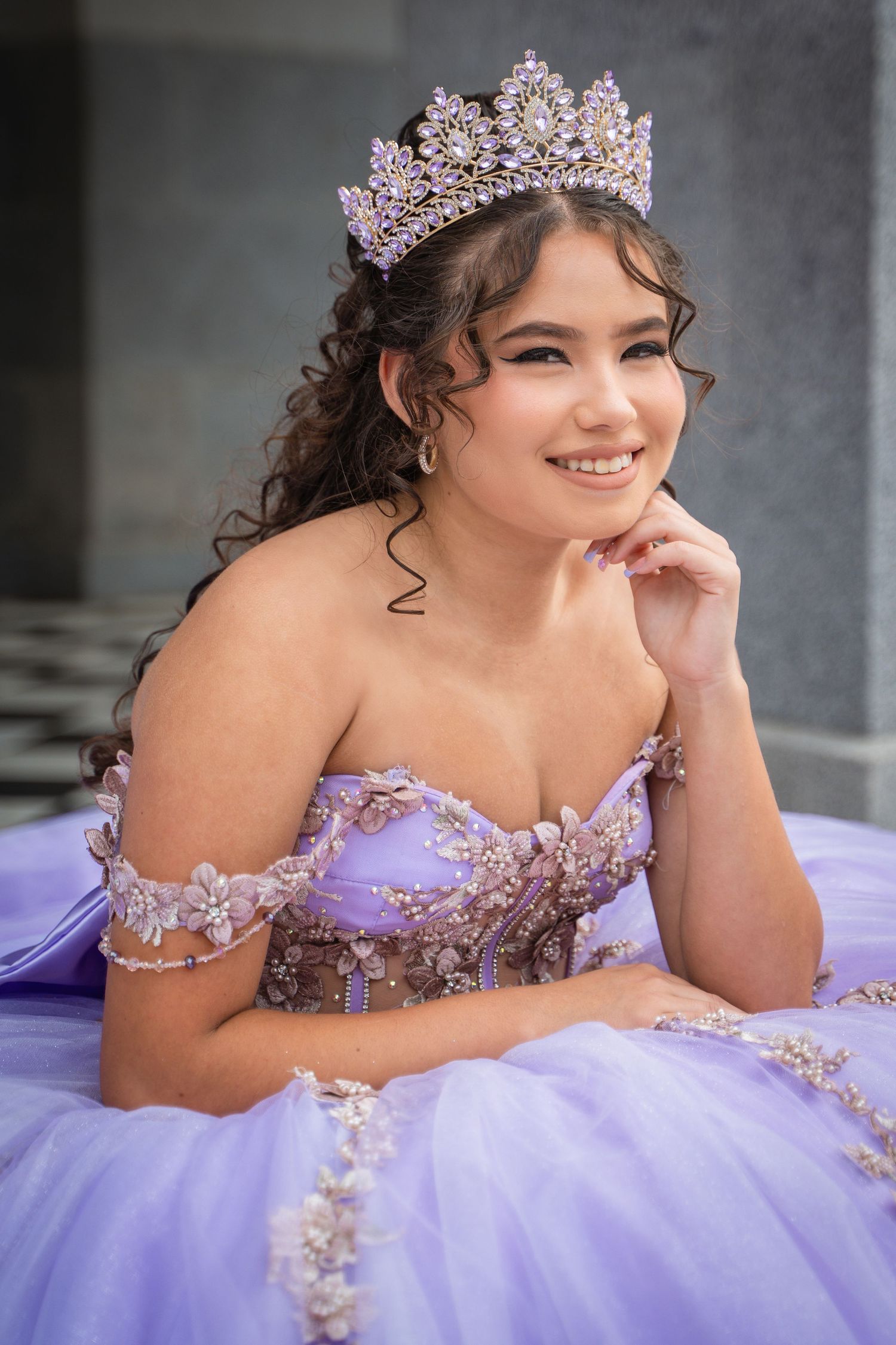 Young woman in lavender quinceañera gown and crystal crown posing elegantly.