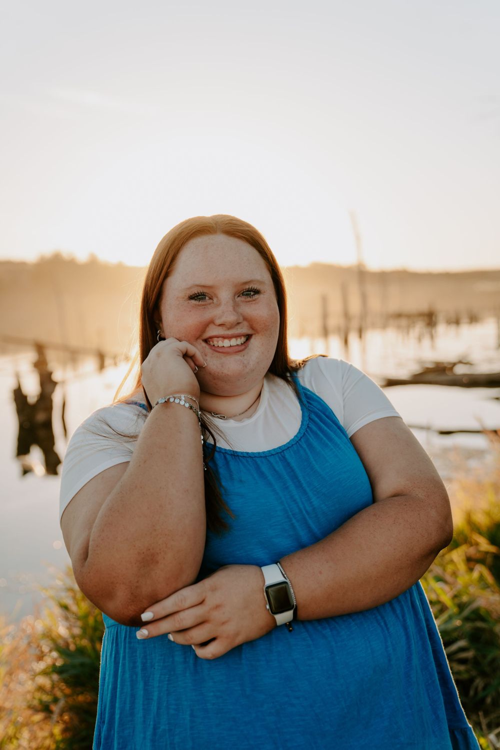 Portrait session at sunset with someone wearing a blue dress and white shirt near a waterfront.