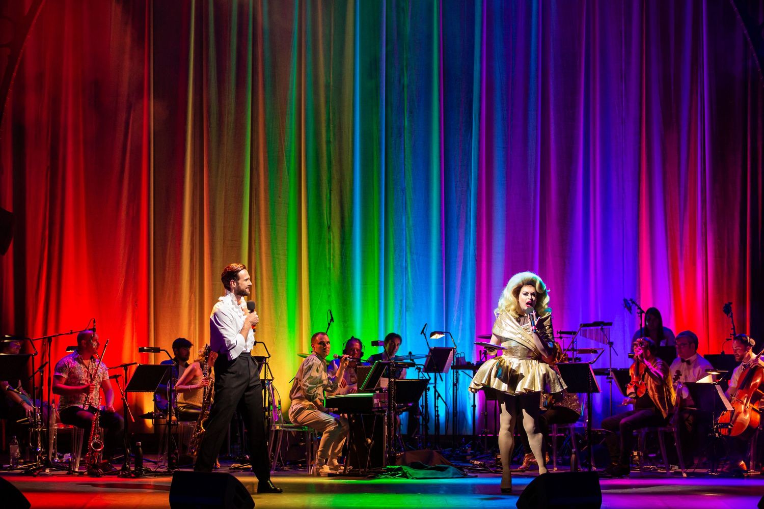 Performers on stage with a stunning rainbow backdrop of vertical light strips.