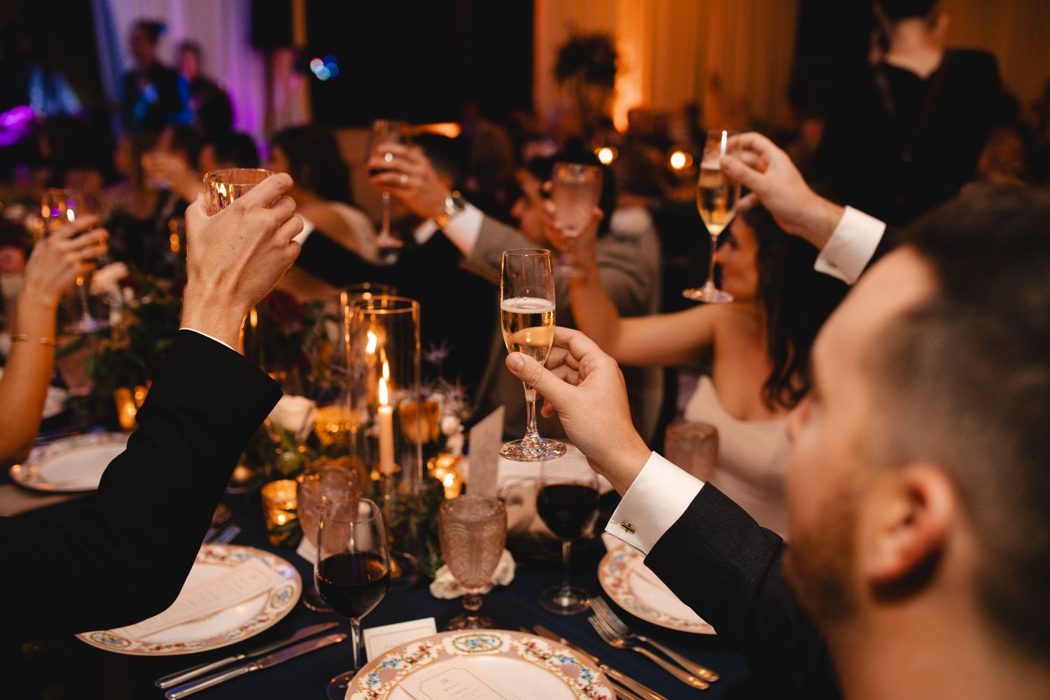 Guests raising champagne glasses in a toast at an elegant candlelit wedding reception dinner.