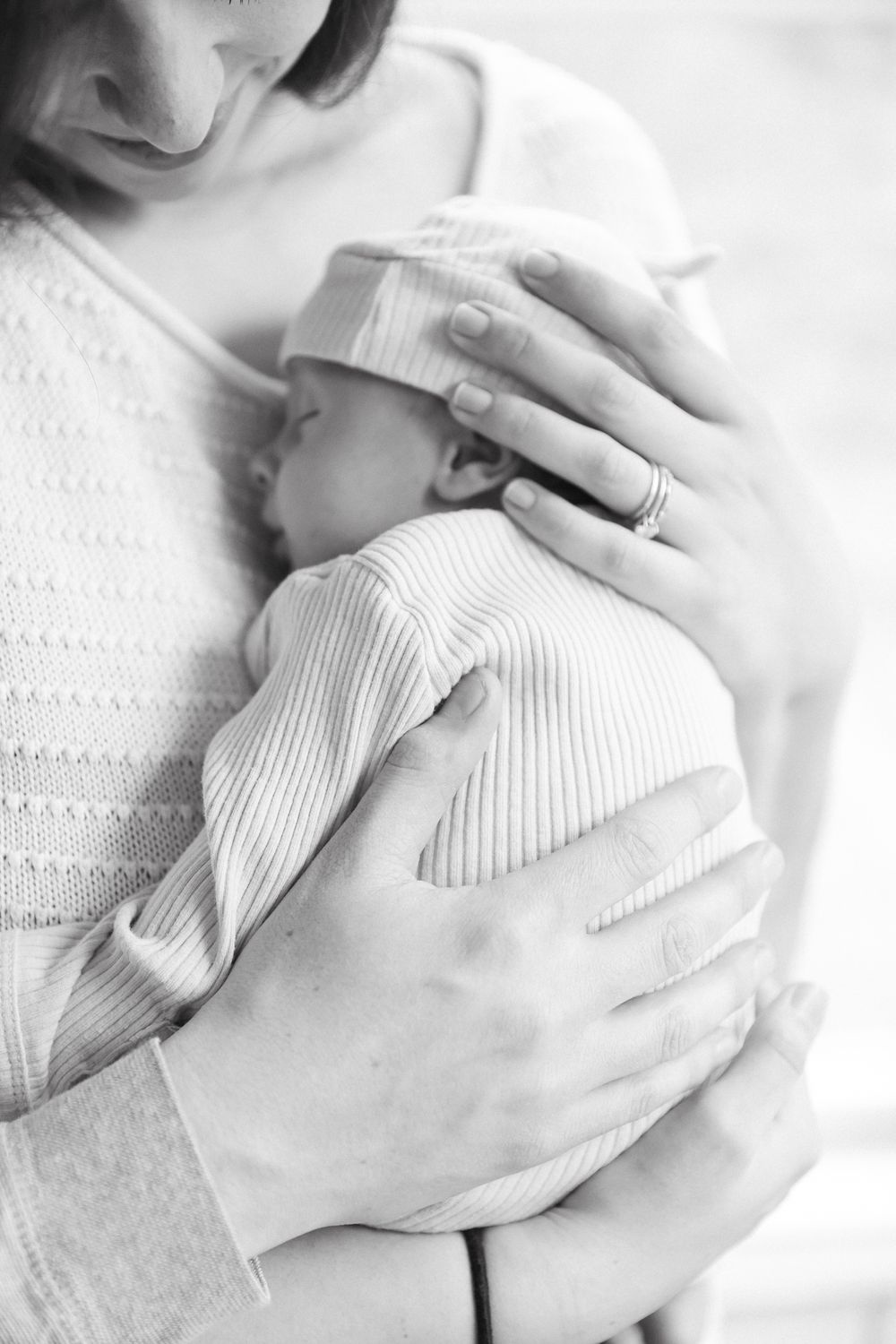 Black and white photo of a mother tenderly cradling her newborn baby wrapped in a striped outfit and hospital hat.
