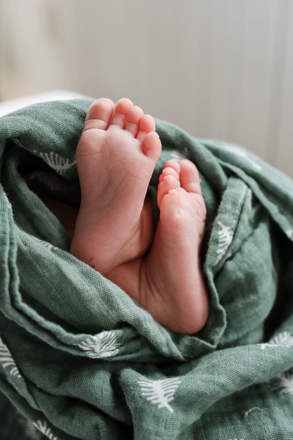Close-up of tiny newborn baby feet wrapped in soft green muslin swaddle blanket.