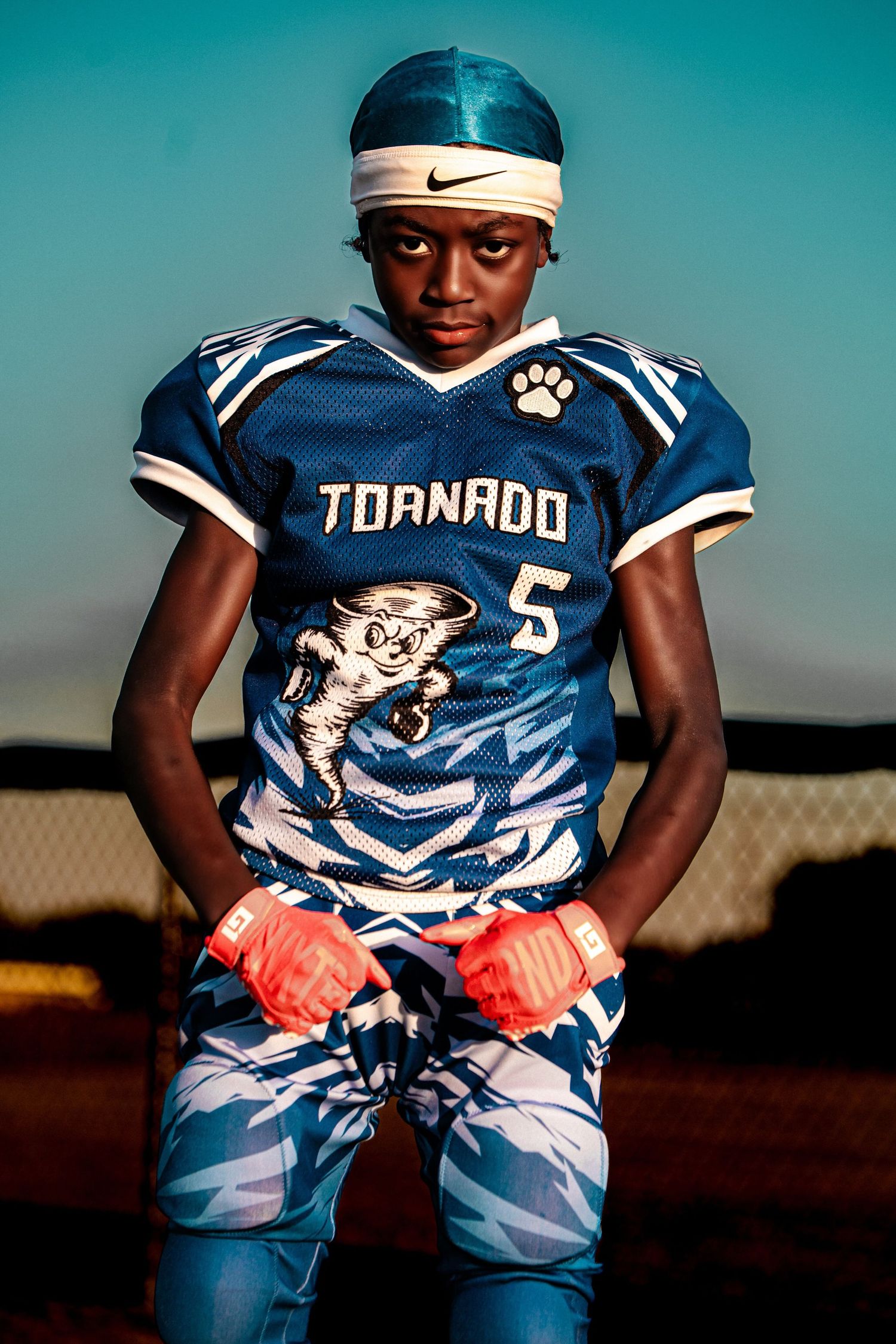 A young football player in a blue Tornado number 5 jersey poses on the field at dusk.