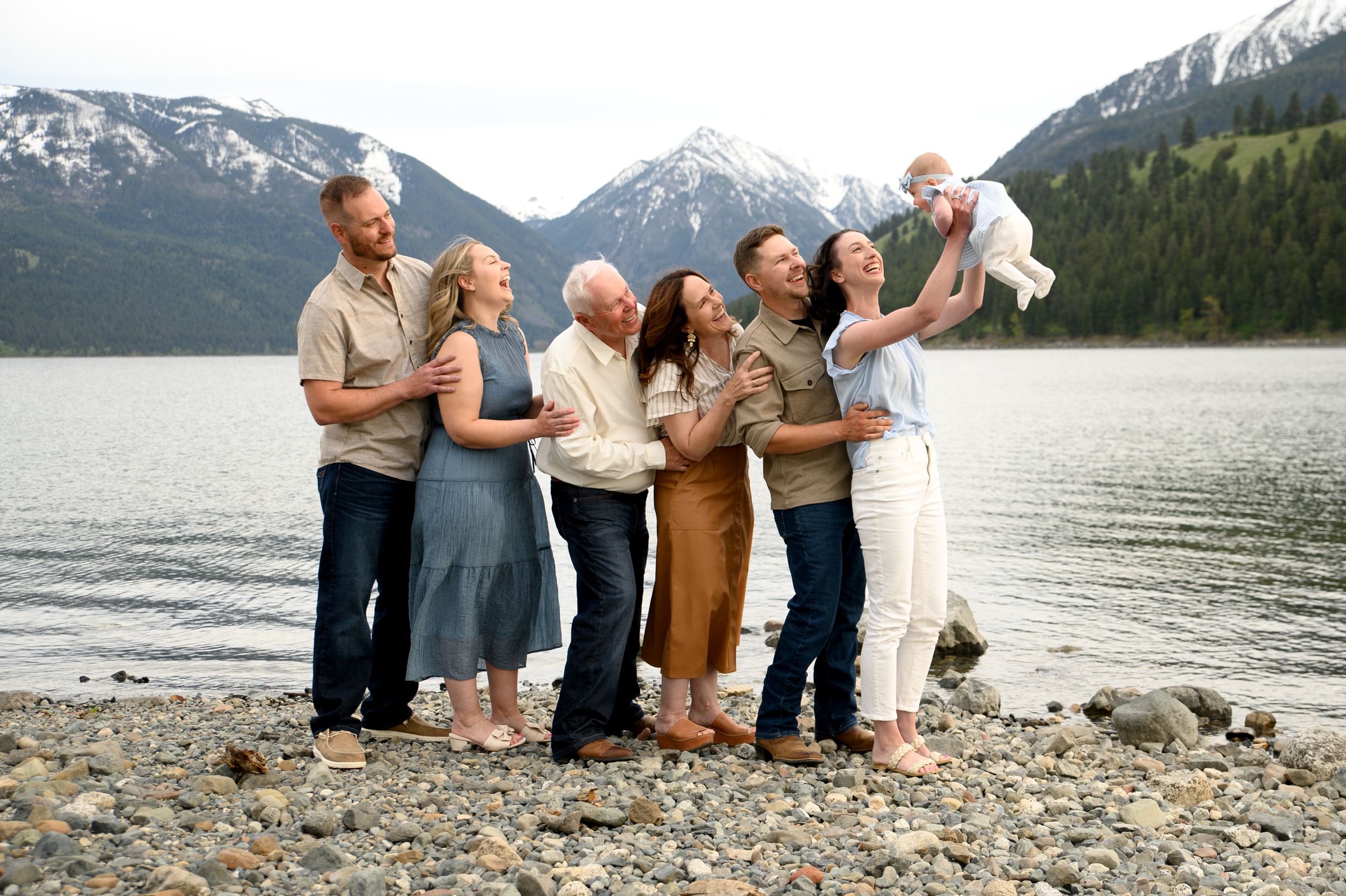 A group poses together on a rocky beach with snow-capped mountains in the background.  Wallowa Lake, Joseph, Oregon