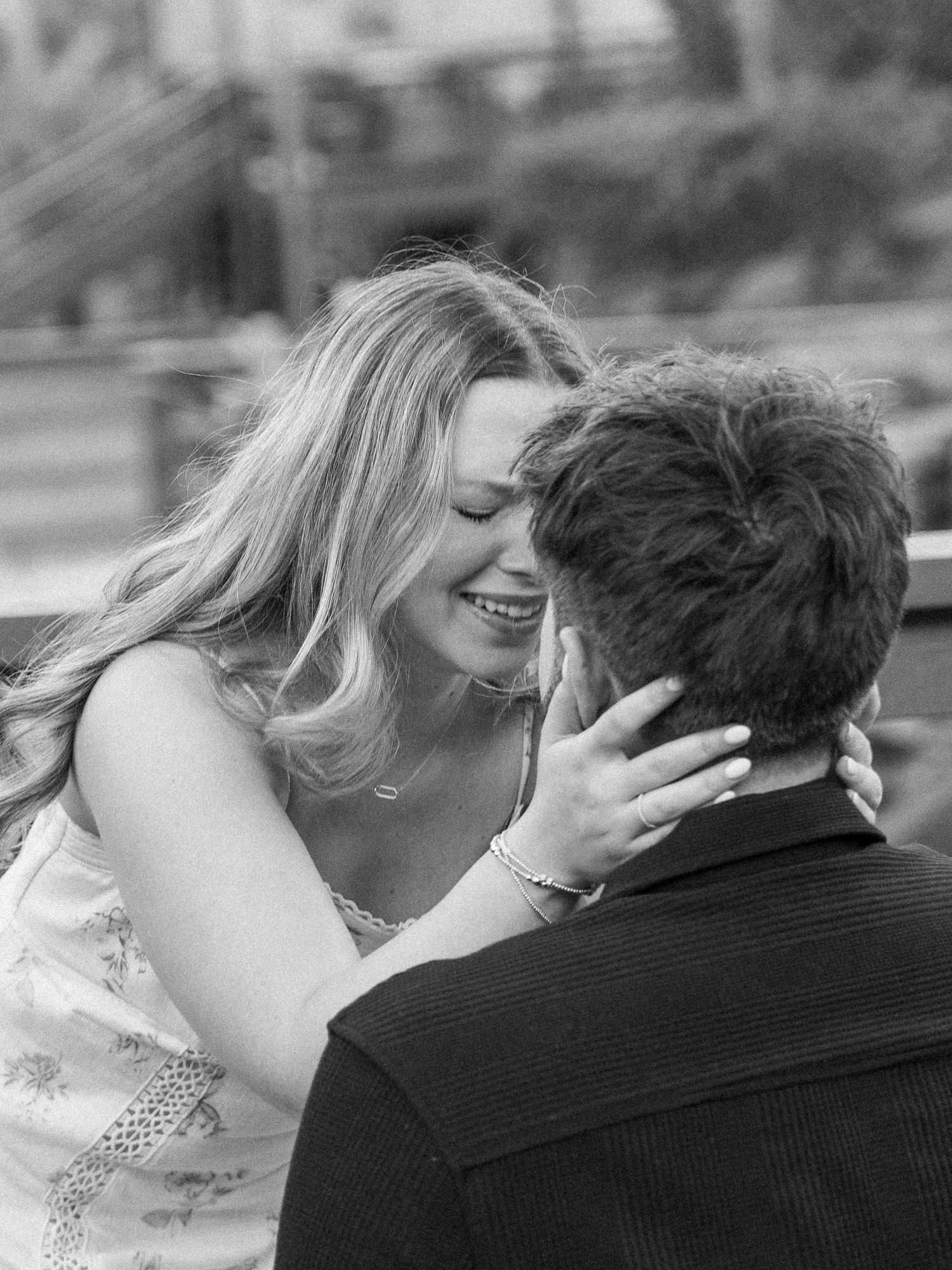 Black and white photo of a smiling woman with long blonde hair embracing a man, sharing a tender romantic moment.