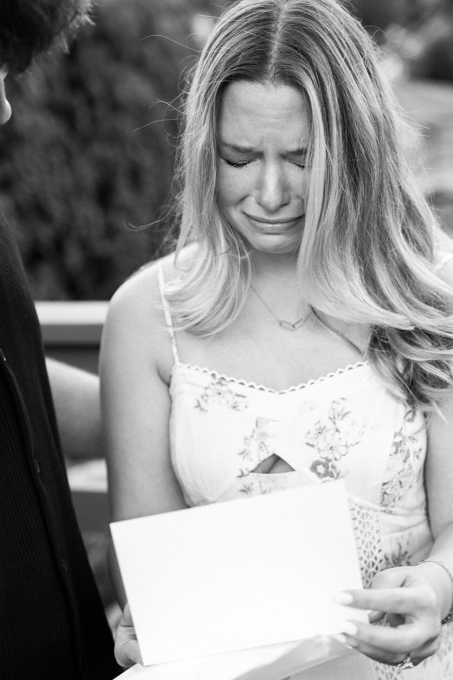 Black and white photo of emotional blonde woman crying while reading a card during a marriage proposal.