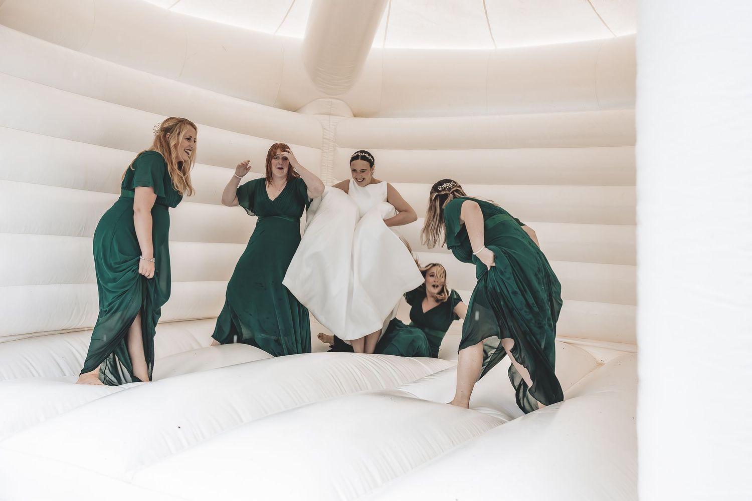 Fun natural moment bride with bridesmaids on bouncy castle.
