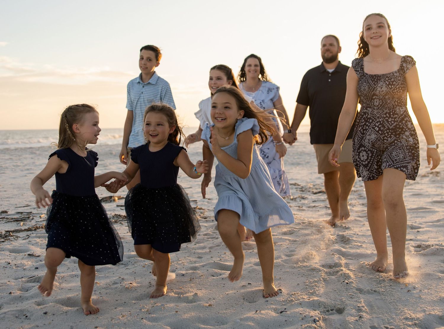 Family with children laughing and running on a sandy beach at sunset, enjoying a fun outdoor photo session in pensacoal, florida