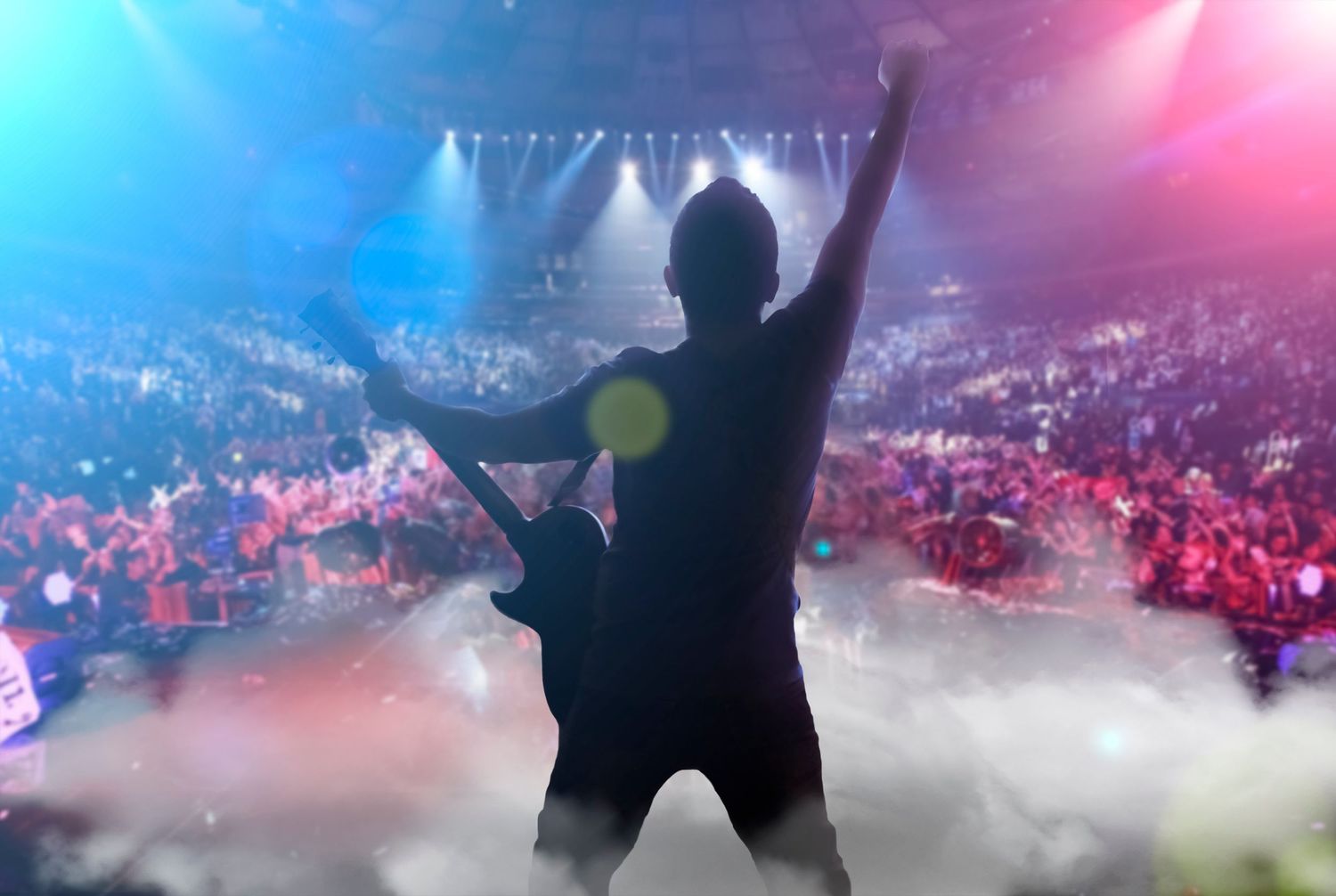 A silhouetted performer stands on stage with colorful blue and pink lighting effects creating a dramatic concert atmosphere.