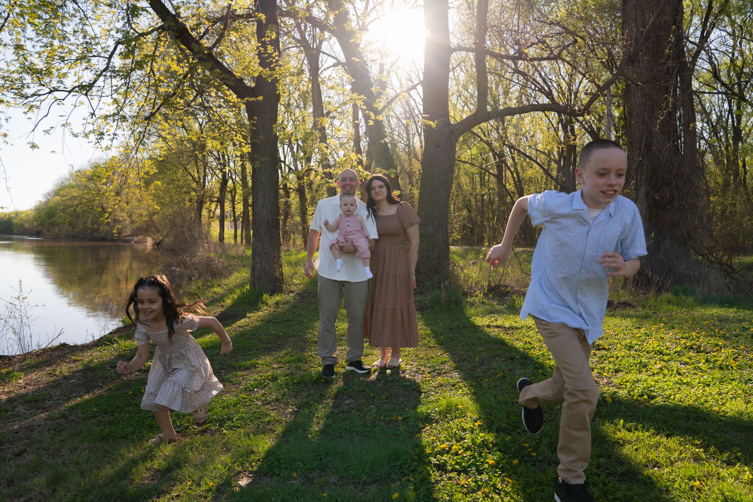 Family with children playing outdoors near a river on a sunny day.