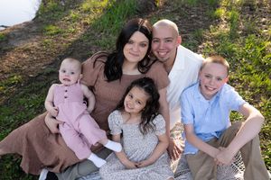 Happy family of five posing outdoors on a blanket in the grass with three children and two parents.