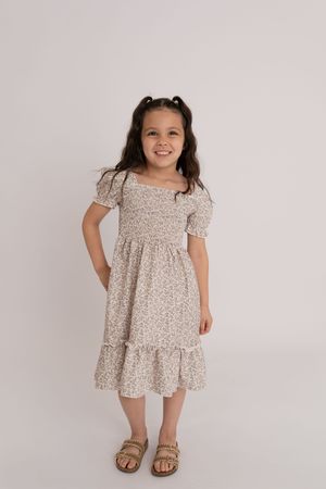 Young girl in a floral smocked midi dress with pigtails smiling against a white studio background.
