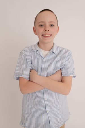 Smiling boy in blue striped shirt with arms crossed poses against white background.