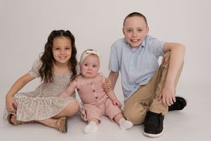 Three siblings pose together in studio, two older kids with baby girl in pink romper.
