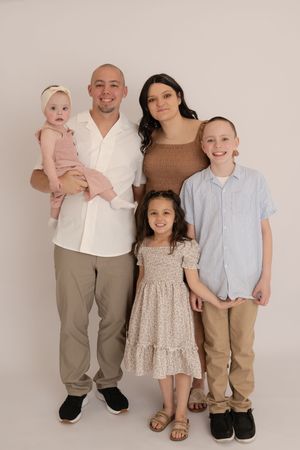 Family of five in coordinating neutral outfits posing together in a professional studio portrait.