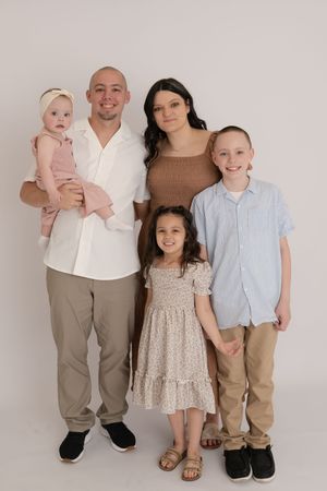 Family of five studio portrait with parents and three young children on white background.