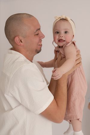 Smiling father holding happy baby girl in pink outfit against white background.