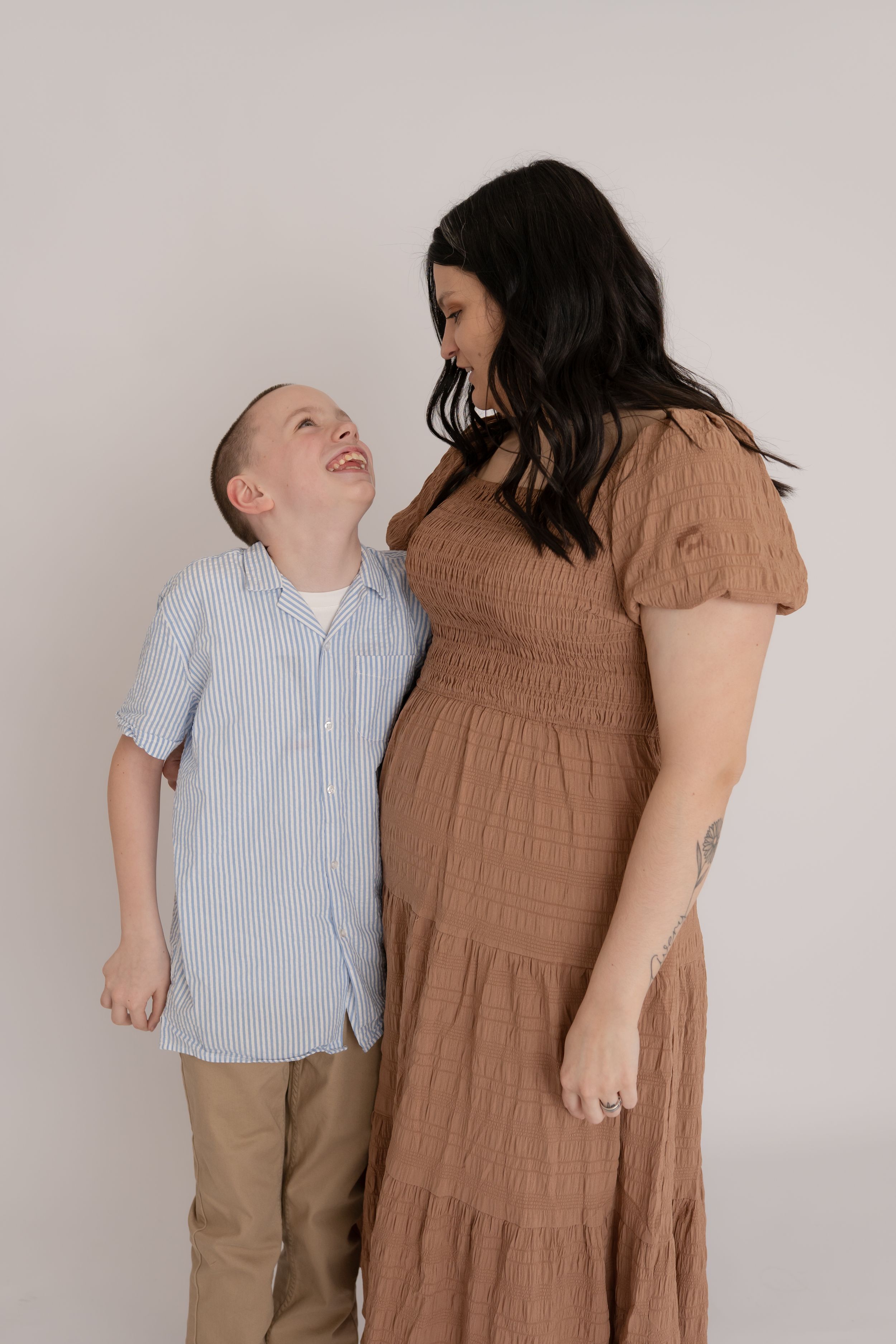 Young boy laughing while looking up at his dark-haired mother in brown dress.