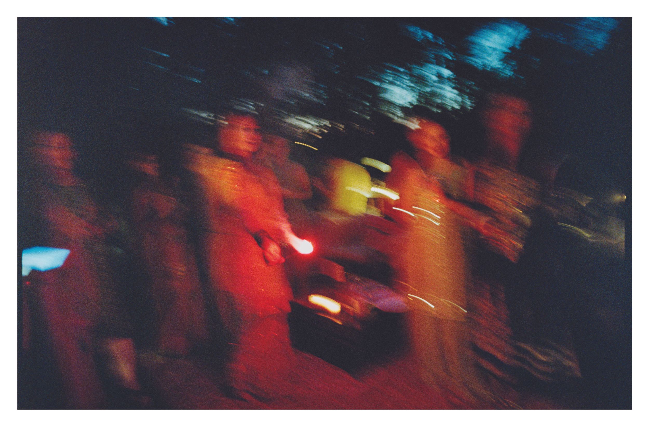 Blurry motion shot of people in orange robes holding candles at nighttime ceremony.