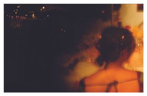 A blurred, moody film photo of a woman in a strapless dress at a nighttime wedding event.