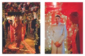 A bride walks through a floral arch as a groom in white stands beneath twinkling fairy lights.