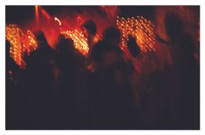 Silhouettes of wedding guests dancing in warm red and orange light at a reception.