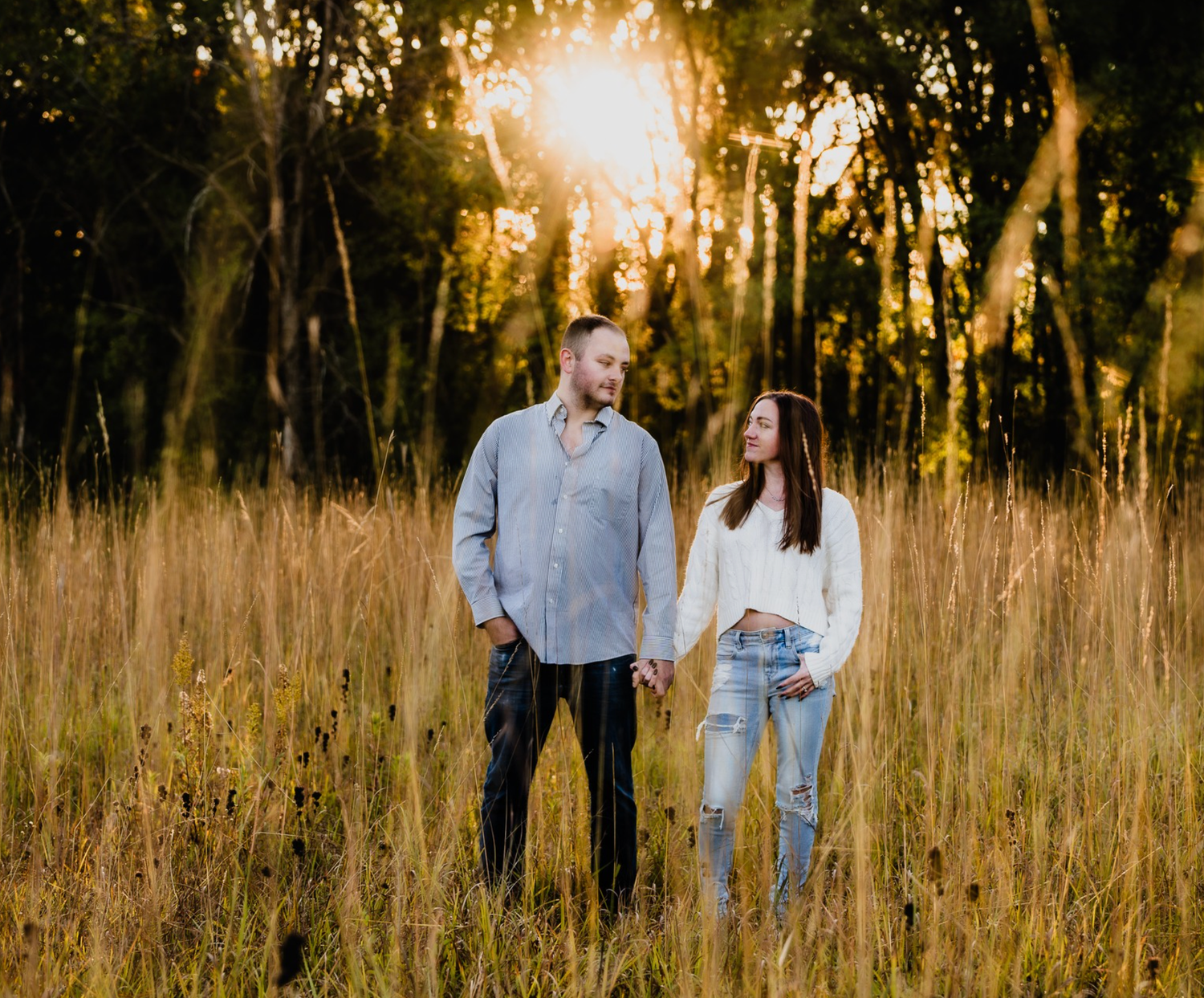 Couple sharing a romantic kiss on a scenic park path surrounded by golden autumn trees at sunset.