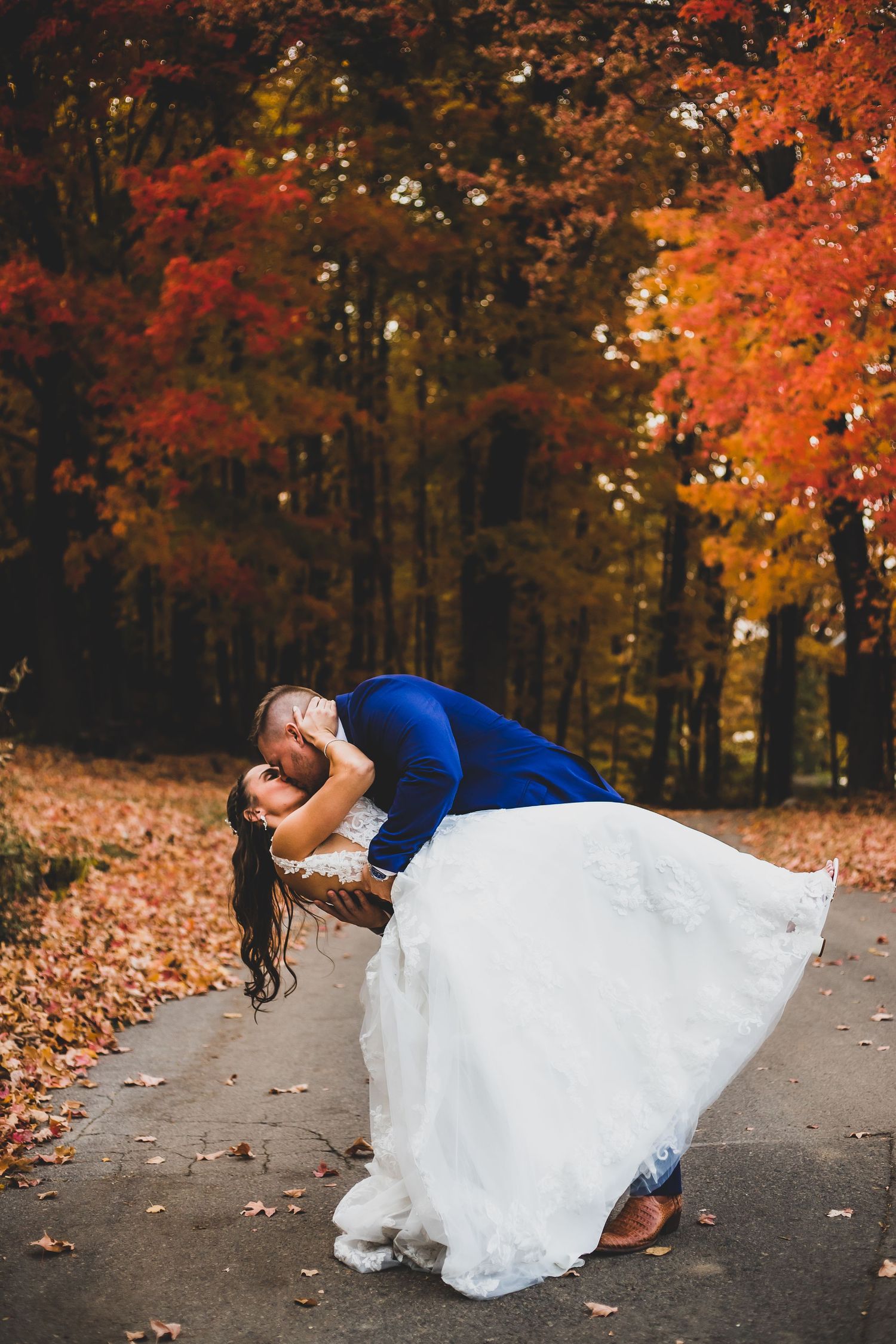 Romantic dip pose with couple in autumn forest surrounded by vibrant red and orange foliage.